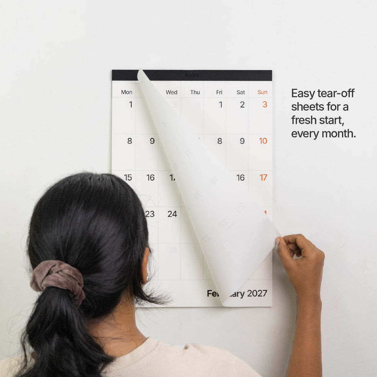 Tear-off sheets: Person tearing off a monthly sheet to reveal February on the Roda 2027 wall calendar.